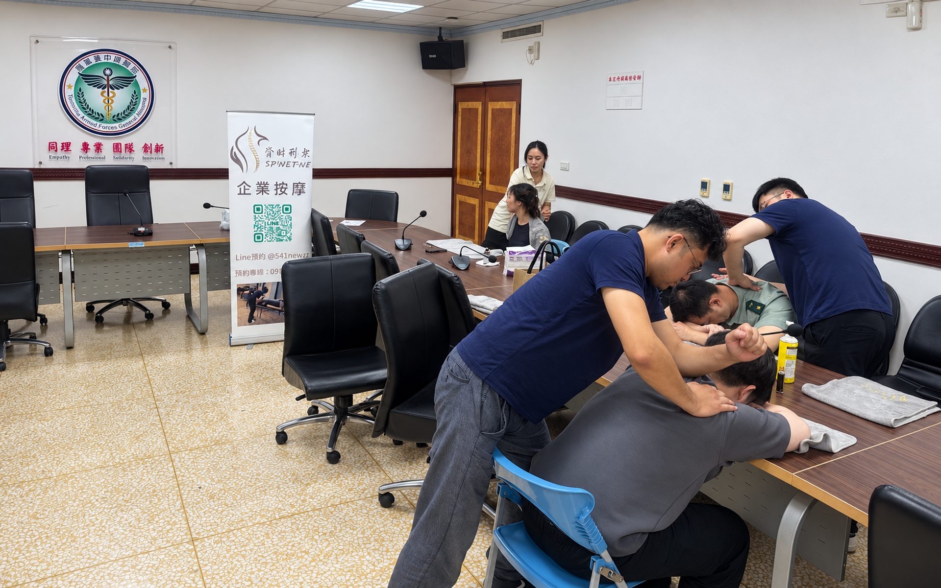 脊時形樂師資在台中醫療院所會議室為同仁做椅式肩頸按摩,旁邊立著企業按摩立牌